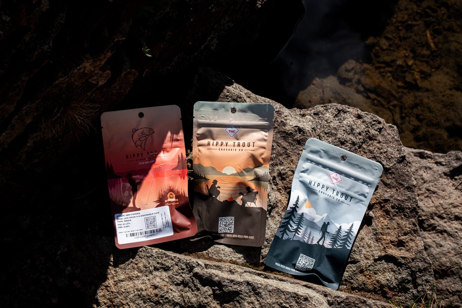 Three Hippy Trout cannabis packs leaning on a sunlit boulder