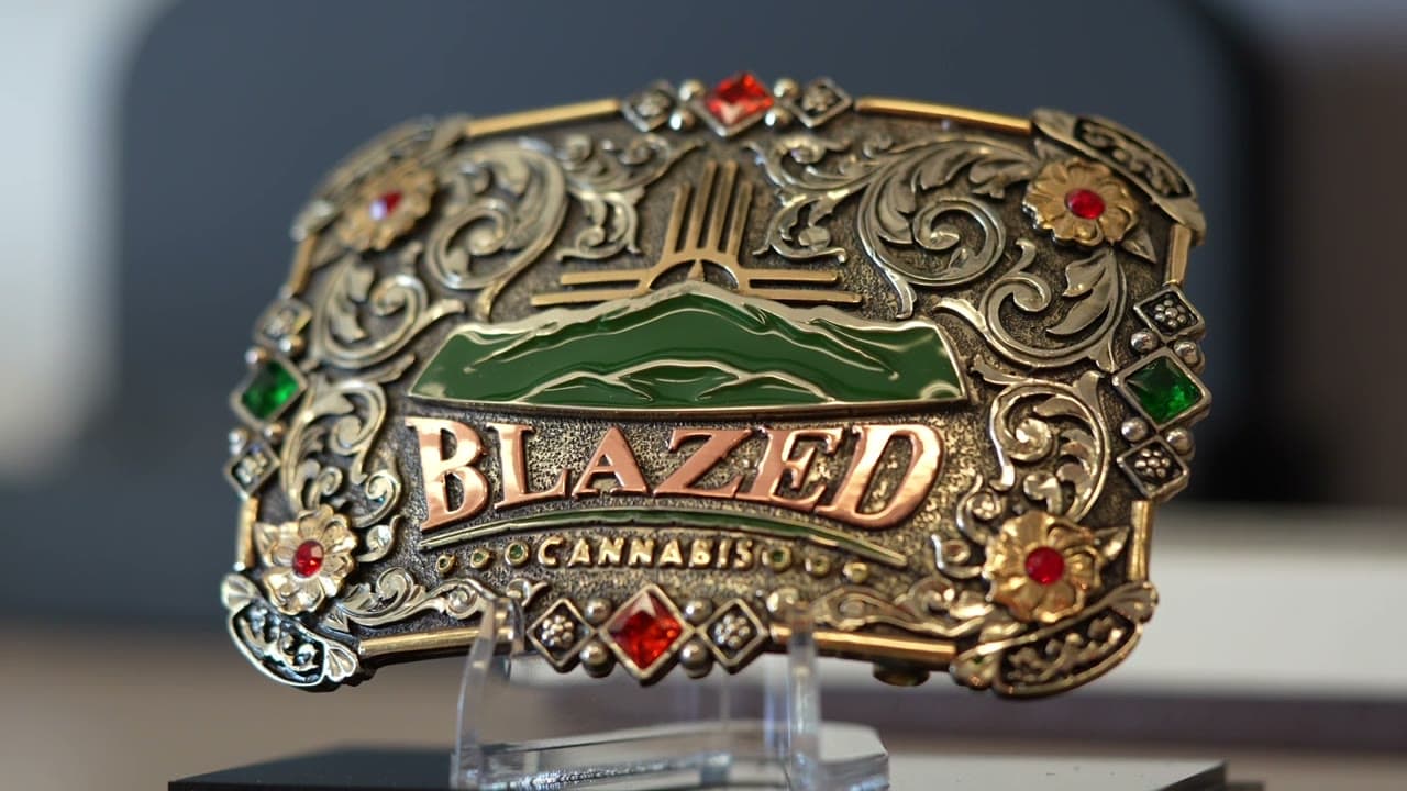 A tooled silver Blazed Cannabis belt buckle with the mountain logo, set on a stand